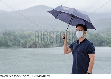Asian Man Wearing Face Mask To Protect From Virus Holding Umbrella When Raining In Monsoon Season.
