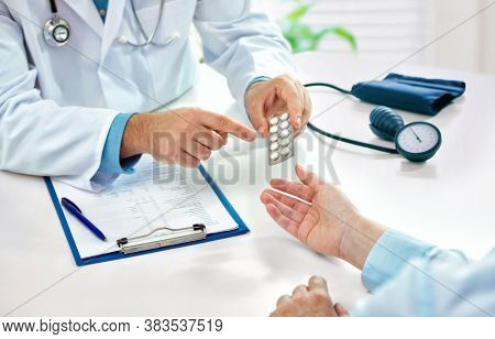 Doctor consulting female patient about pills and dicsussing health treatment sitting in the office at the desk. Medicine and health care concept