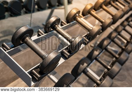 Group Of Black Metal Dumbbells On Rack In Exercise Gym. Weight Training Equipment In Sport Fitness C