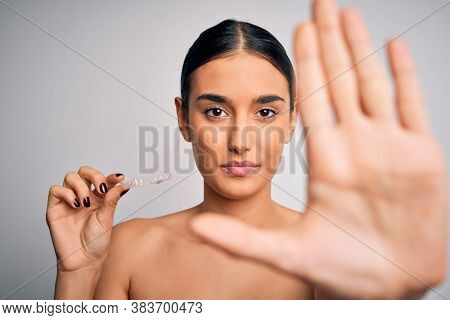 Young beautiful brunette woman holding dental aligner orthodontic to teeth corretion with open hand doing stop sign with serious and confident expression, defense gesture