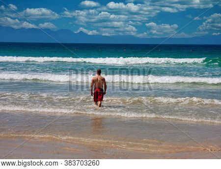 muscular caucasian man walking into the ocean in Cape Town