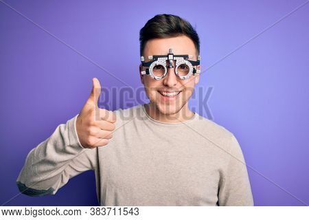 Young handsome caucasian man wearing optometrical glasses over purple background doing happy thumbs up gesture with hand. Approving expression looking at the camera showing success.