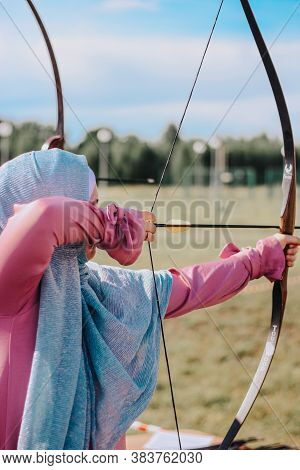 A Girl In A Headscarf Hijab Shoots From A Bow. Weapon Bow. Bow And Arrows. Archery. Archery On The F