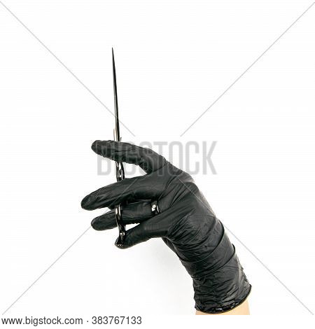 Gloved Hand Holding A Black Scisors On An Isolated White Background.