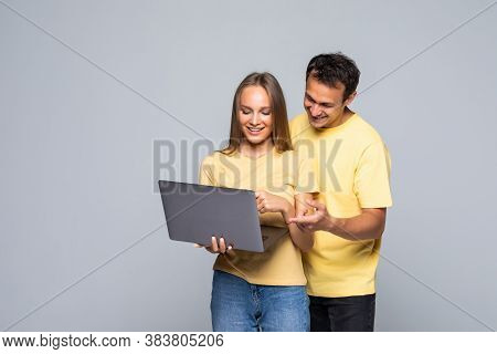 Portrait Of A Happy Young Couple Using Laptop Computer While Standing Over Gray Wall Background