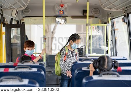 Kids With Medical Mask Coming Inside School Bus And Sitting On Seats While Maintaining Social Distan