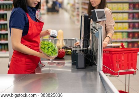 Cashier beeping goods for customer at cash register in modern supermarket