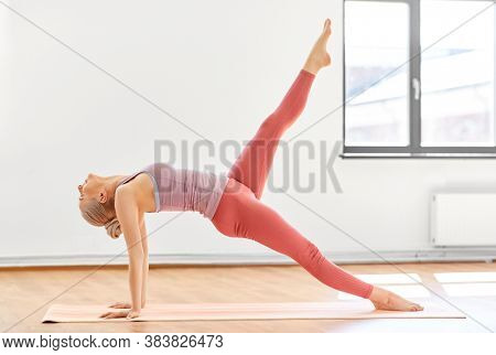 fitness, people and healthy lifestyle concept - young woman doing yoga in upward plank pose with one leg up at studio