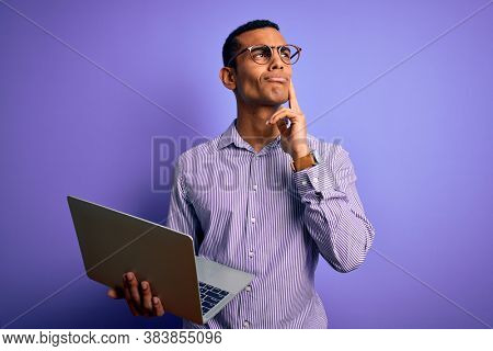 Young handsome african american business man working using laptop over purple background serious face thinking about question, very confused idea