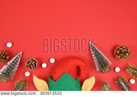 Seasonal Flat Lay With Christmas Elf Hat And Ears, Snall Pine Trees And Cones And White Snowballs At