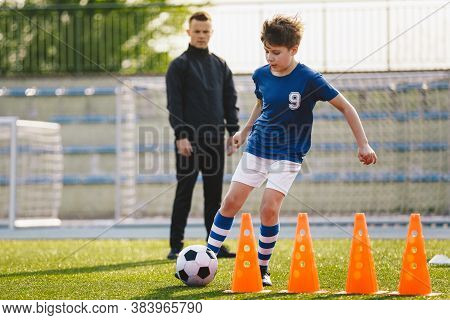 Kid Soccer Player Dribbling Through Cones. Boy In Soccer Uniform Practice With Ball. Child Kicking B