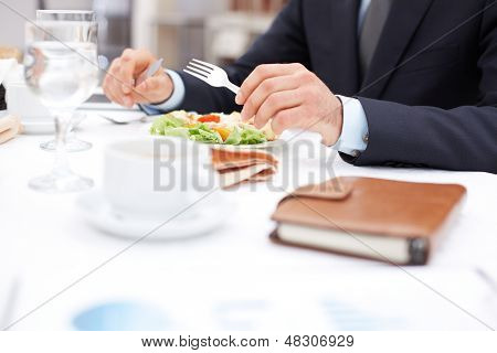 Næroptagelse af forretningsmand hænder holder kniv og gaffel over vegetabilske salat under firma frokost