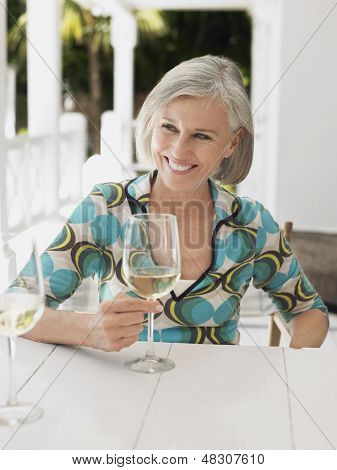 Portræt af en midten alderen kvinde holde glas vin på verandah tabel