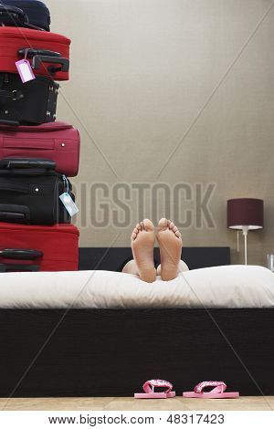 Sección baja de mujer acostada en una cama próxima a pila de maletas