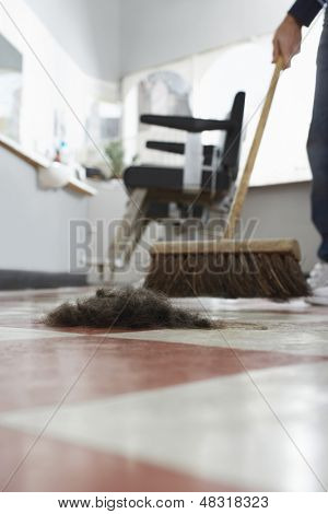 Parrucchiere spazzare ritagli di capelli sul pavimento nel negozio di barbiere