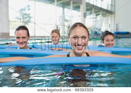 Female fitness class doing aqua aerobics with foam rollers in swimming pool at the leisure centre
