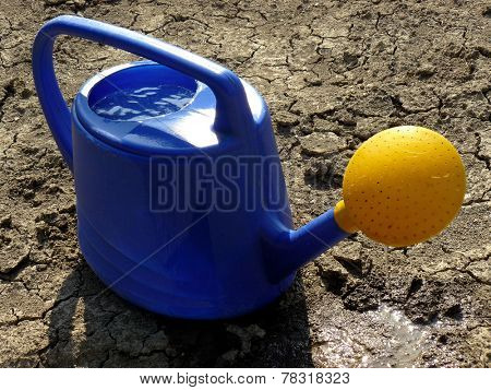 watering can full of water on dry cracked soil