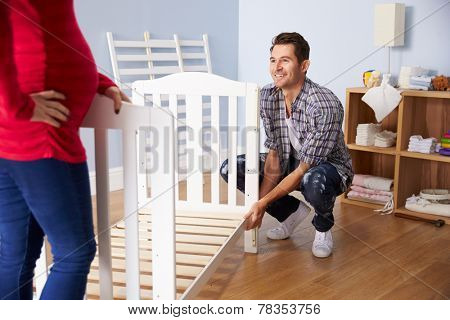Couple With Pregnant Wife Assembling Cot In Nursery