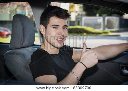 Happy young man or teenager doing thumb up driving car
