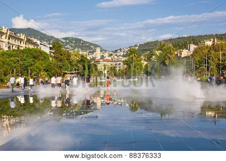 NICE, FRANCE - OCTOBER 2, 2014: People walking through soaking fountain on Promenade du Paillon reflecting the city and surrounding hills.