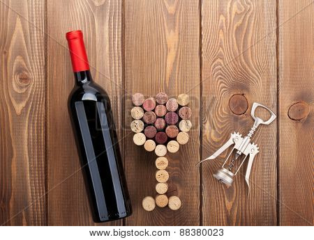 Red wine bottle, glass shaped corks and corkscrew. View from above over rustic wooden table background