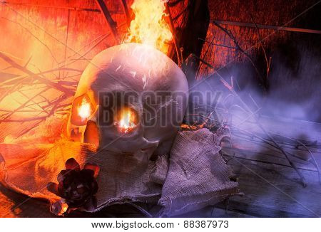 Anatomic white skull lying on wooden old surface with tree branches, fog, cloth & fantasy fire effect eyes composition.