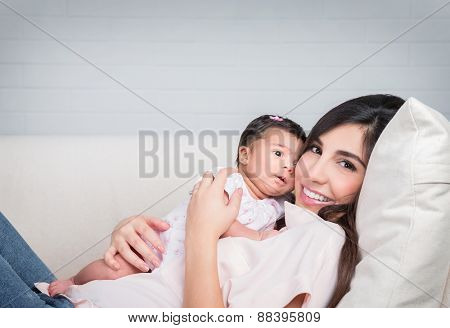 Happy mother with baby lying down on the couch at home, cheerful woman playing with her adorable daughter, love and happiness concept
