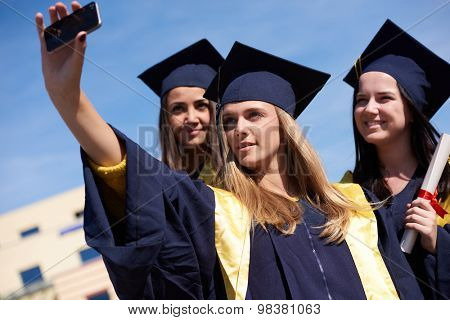 Capturing a happy moment.Students group  college graduates in graduation gowns  and making selfie photo
