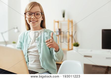 Liking the information. Adorable cheerful emotional girl holding her thumb up while enjoying her time searching interesting things online