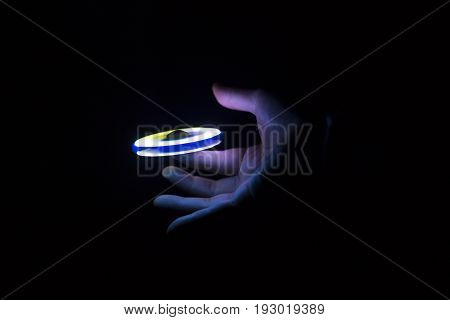 Play Fidget spinner spinning and Hand on dark background With Ligtht