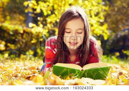 girl lying on fallen leaves  in the park and reading a book. reading, learning and education in autumn
