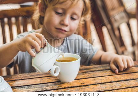 Happy Nice Boy Pours Honey Into The Tea In Summer Green Garden. Portrait. Outdoor