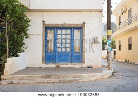 Elounda, Crete, Greece - June 12, 2017: Abandoned house facade in a corner of the street, windows covered by newspapers