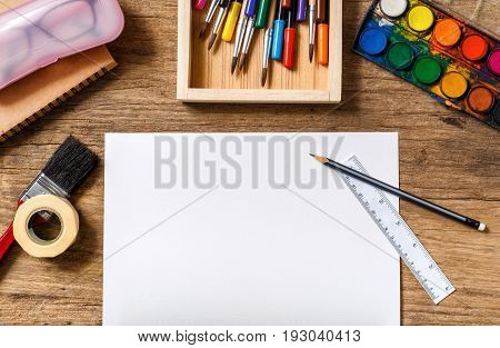 Piece of white paper and various colorful drawing tools on wooden background Top view.