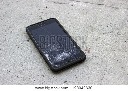 The phone with the broken screen lies on the asphalt, close up