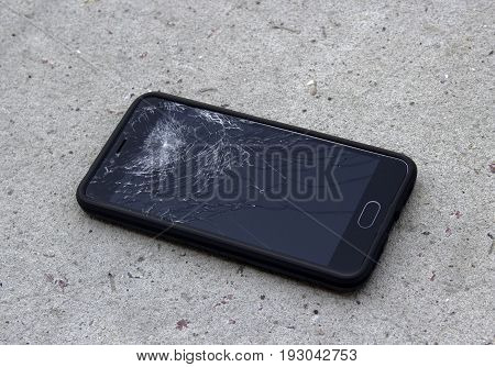 The phone with the broken screen lies on the asphalt