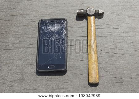 Hammer next to the phone with a broken screen on a tree background