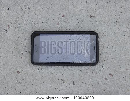 The phone with the broken screen lies on the asphalt horizontally