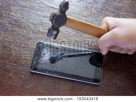 The hand swings a hammer on the phone with a broken screen
