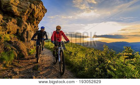Mountain biking women and man riding on bikes at sunset mountains forest landscape. Couple cycling MTB enduro flow trail track. Outdoor sport activity.