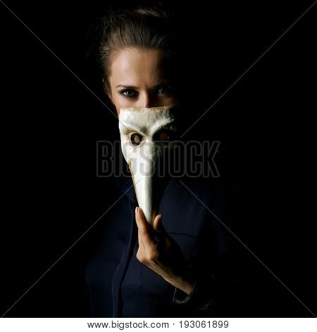 Coming out into the light. Portrait of woman in the dark dress isolated on black hiding behind Venetian mask