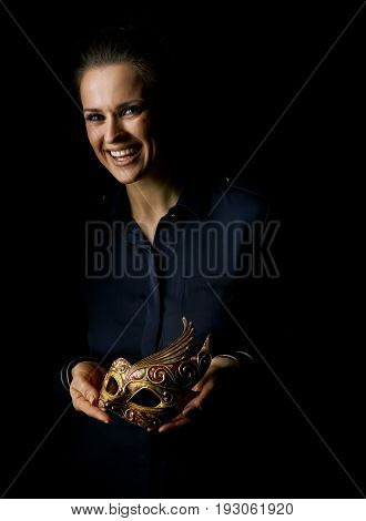 Coming out into the light. Portrait of smiling woman in the dark dress isolated on black showing Venetian mask