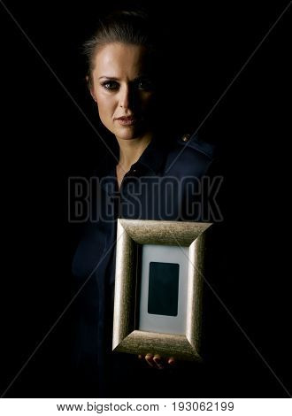 Coming out into the light. Portrait of woman in the dark dress isolated on black showing a photo frame