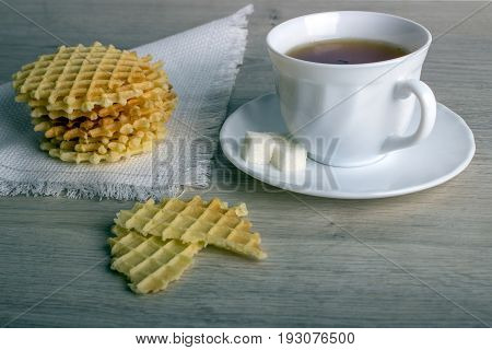 Breakfast With White Cup Of Black Tea With Waffles Stack On Napkin And Pieces Of Waffle On Wooden Su