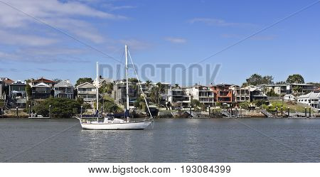 BRISBANE, AUSTRALIA - June 22, 2017: Two masted sailing boat moored in the Brisbane River in front of the million dollars mansions of the Eastern suburb of Norman Park Brisbane Australia