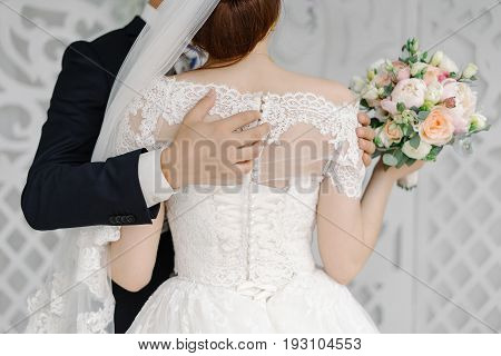 Groom passionately hugs beautiful bride wth white veil the back view