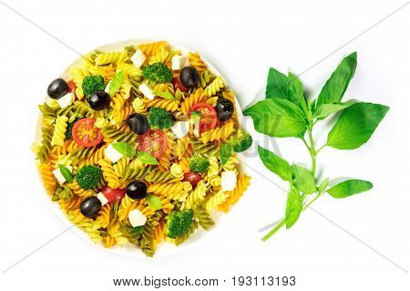 A photo of a plate of pasta salad with basil leaves, shot from above on a white background with a place for text