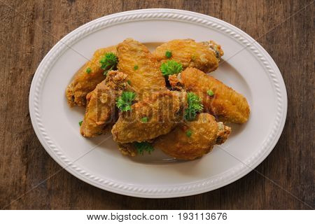 Fried chicken wings on white plate put on rustic wood table. Homemade fried chicken wing look so delicious and crispy. Top view of deep fried chicken wing decorate with scallion and parsley on white plate ready to served.