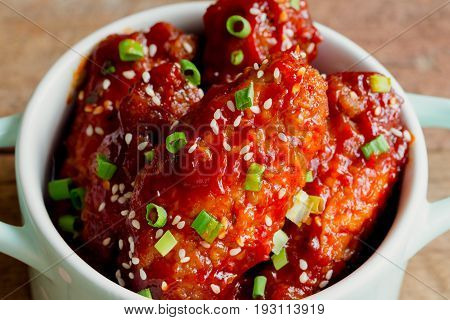 Korean fried chicken wings sprinkled with sesame and scallion in little bowl. Korean barbecue chicken wing delicious moist and spicy. Close up on fried chicken wings in Korean style on wood table. Homemade Korean fried chicken.