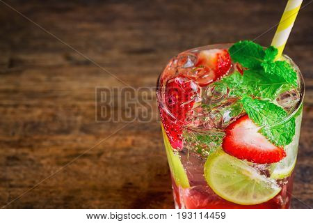 Strawberry lemon lime soda in clear glass on rustic wood table. Homemade strawberry soda ingredients with strawberry lemon or lime and mint leaf. Homemade infused water close up concept. Strawberry and lemon soda on plank with copy space.